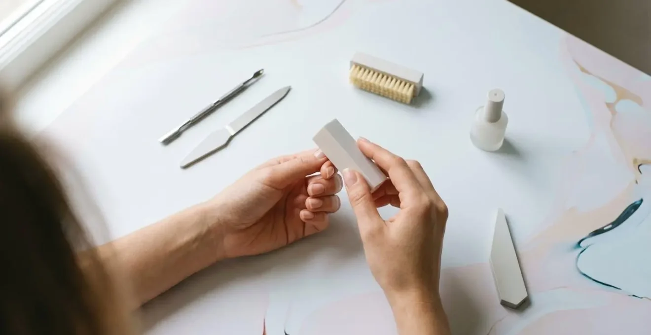 Gros plan sur des mains féminines préparant des ongles pour une pose de vernis semi-permanent, avec outils de manucure professionnels