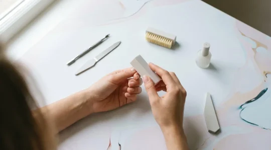 Gros plan sur des mains féminines préparant des ongles pour une pose de vernis semi-permanent, avec outils de manucure professionnels